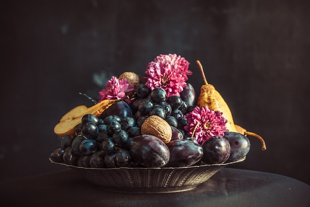 The fruit bowl with grapes and plums against a dark wall