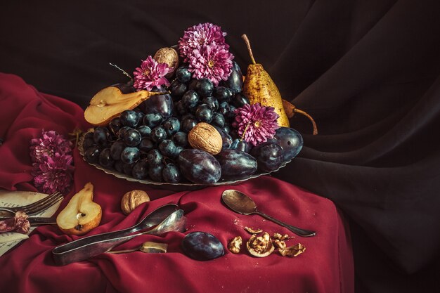 The fruit bowl with grapes and plums against a maroon tablecloth