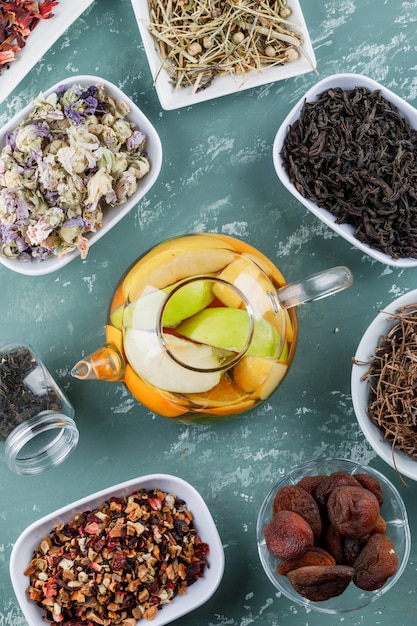 Free photo fruit infused water in a teapot with dried apricots, herbs, cherry stalks top view on a plaster surface