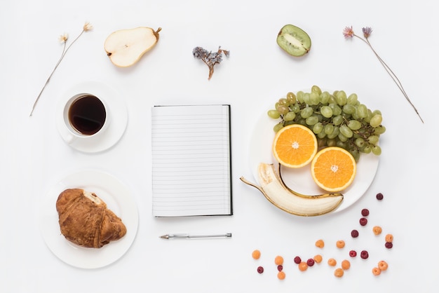 Free Photo fruits arranged a human face on plate with croissant; coffee and dried flowers on white background