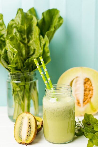 Fruits near herbs and glass with cocktail and straws