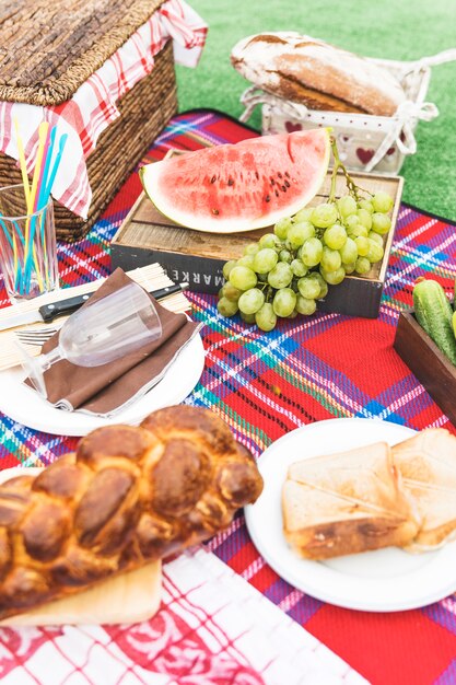 Fruits; sandwiches and baked braided bread loaf on blanket