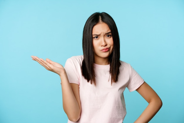 Frustrated asian girl shrugging looking bothered and annoyed cant understand smth standing in tshirt...