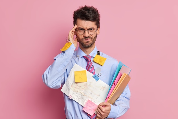 Free Photo frustrated displeased office worker has headache keeps hand on temple looks discontent at camera being tired because of paper work poses 