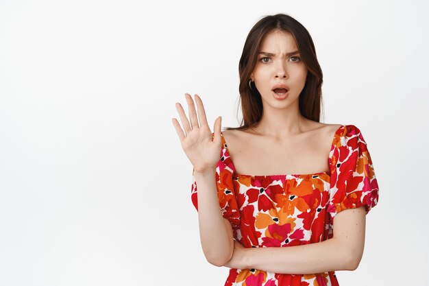 Frustrated girlfriend showing stop gesture waving to reject something say no standing angry against white background in red floral dress