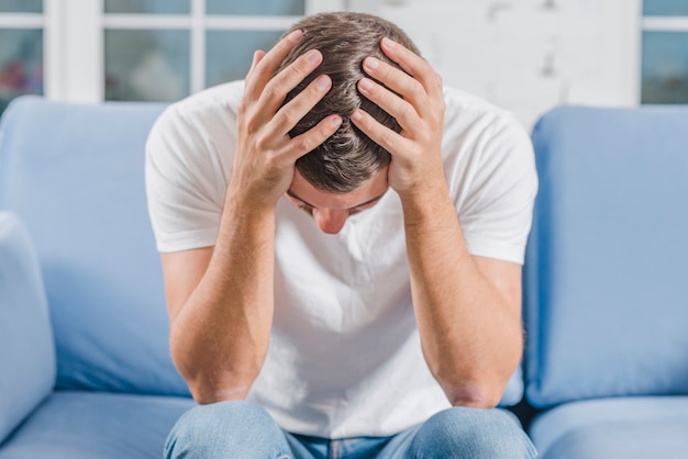 Free photo frustrated man suffering from headache sitting on sofa