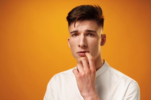 Frustrated and nervous young man biting nail against yellow background