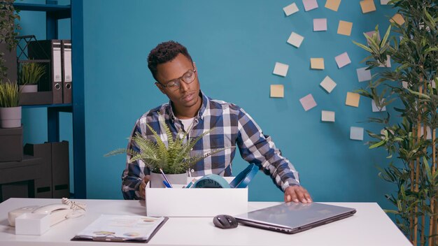 Frustrated person packing up belongings in box after getting fired from office job. Unhappy man feeling worried about unemployment, gathering things after being dismissed and discharged.