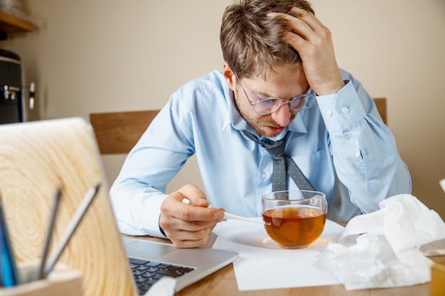 Frustrated sad unhappy sick young man massaging his head while sitting at his working place in office