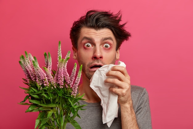 Free Photo frustrated unhealthy man suffers from allergic disorder, eyes start to water, has runny nose, holds handkerchief and looks in despair , sensitive to seasonal allergens has shortness of breath