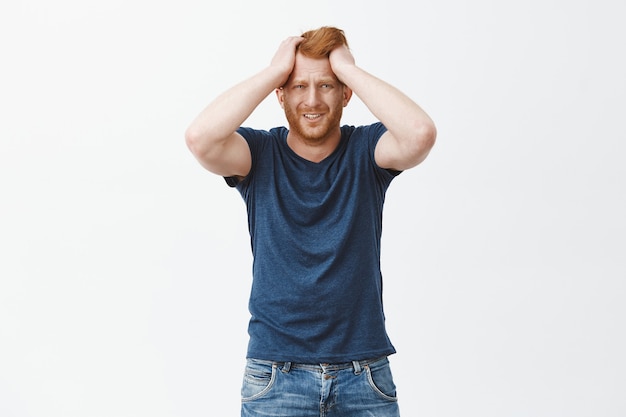 Frustrated upset redhead euroepan man in trouble, holding hands on head, frowning and grimacing from sadness and grief