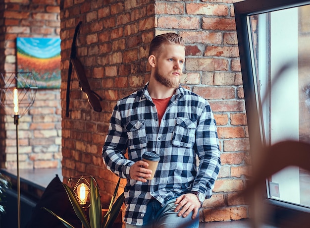 Free Photo the full body image of blond hipster male drinks coffee in a room with loft interior.