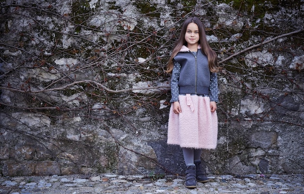 Full body portrait of teenager female in pink skirt and grey jacket on frozen rock background.