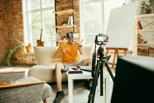 Free photo full of emotions. caucasian male blogger with professional camera recording video review of vr glasses at home