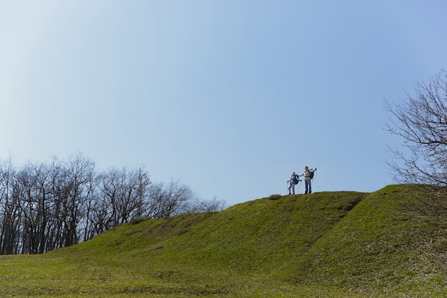 Free photo full and free breathing. aged family couple of man and woman in tourist outfit walking at green lawn near by trees in sunny day. concept of tourism, healthy lifestyle, relaxation and togetherness.