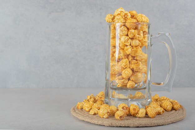 Full glass mug on a trivet ringed with caramel flavored popcorn on marble table.