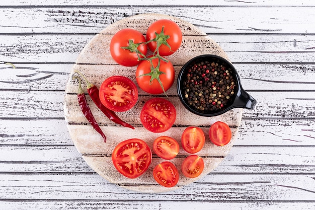 Free photo full and half tomatoes on white board dry red hot chili pepper isolated and black pepper powder in black bowl on white wooden surface