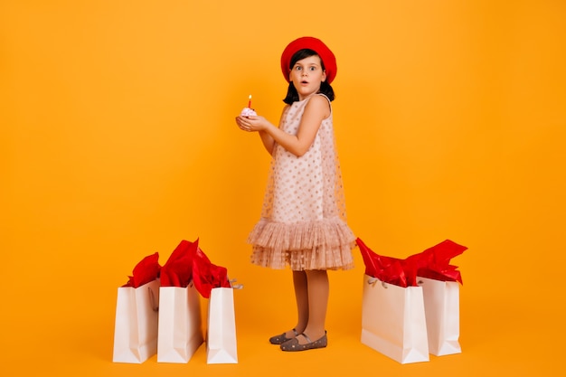 Full lengh shot of little girl with shopping bags. cute kid in red french beret isolated on yellow wall.