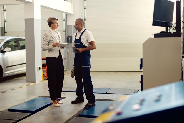 Full length of African American mechanic and businesswoman communicating at auto repair shop