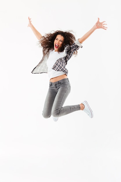 Free Photo full length cheerful curly woman jumping  and looking away over white wall