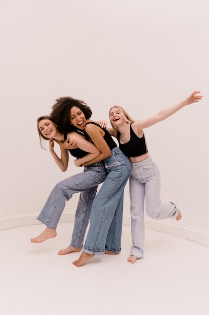 Full length cheerful young caucasian and african girls in casual clothes fool around on white background