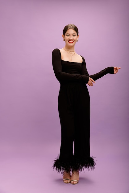 Full length glamorous young caucasian brunette lady in black suit smiles at camera on purple background Fashion concept