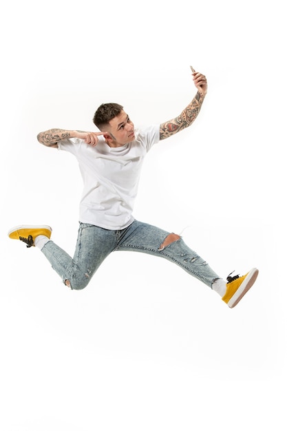 Free Photo full length of handsome young man taking phone while jumping against orange studio background.