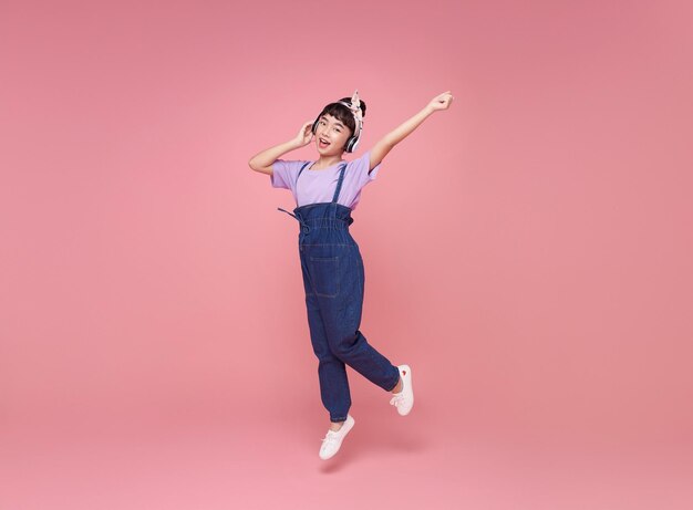 Full length happy asian teen children girl wearing headphones listening to music and jumping