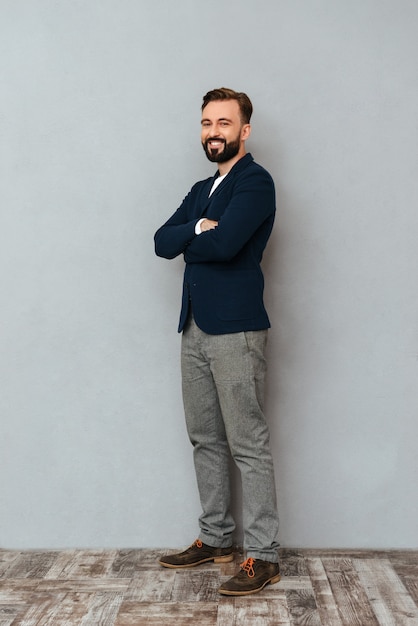 Free Photo full length image of bearded man in busines clothes posing with crossed arms and looking at the camera over gray 