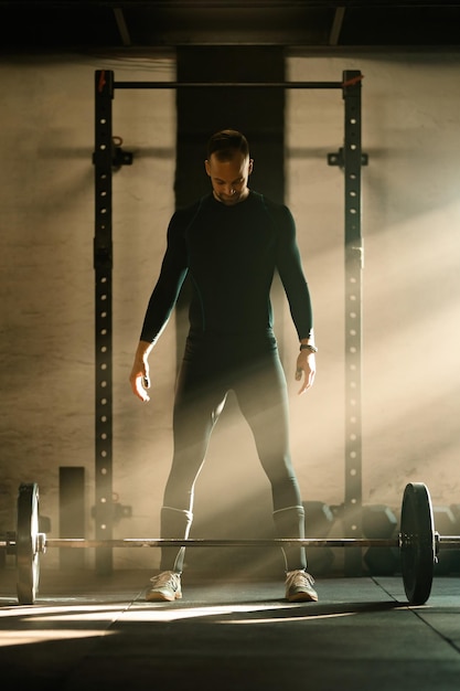 Free photo full length of muscular build man concentrating before lifting a barbell during strength training in a gym