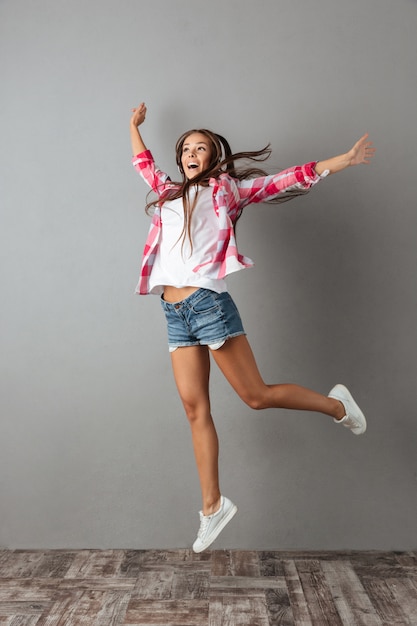 Full-length photo of pretty young woman in earphones listening to music and jumping