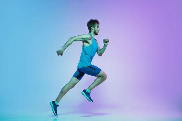 Free photo full length portrait of active young caucasian running, jogging man on gradient studio in neon light