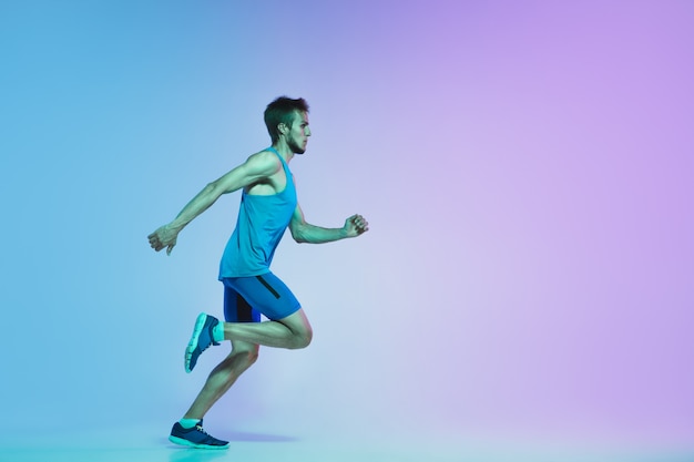 Full length portrait of active young caucasian running, jogging man on in neon