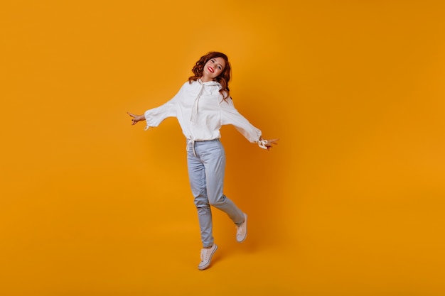 Full-length portrait of amazing slim girl with ginger hair. Caucasian romantic woman dancing on yellow wall.