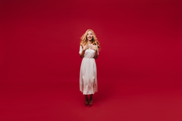 Free photo full-length portrait of cheerful woman in white dress.  charming long-haired girl isolated on red wall.