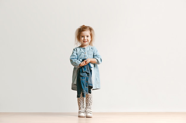 Full length portrait of cute little kid girl in stylish jeans clothes and smiling, standing on white. Kids fashion concept