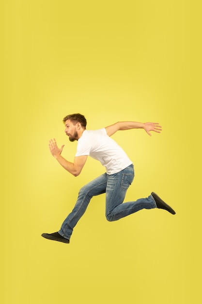 Full length portrait of happy jumping man isolated on yellow background. Caucasian male model in casual clothes. Freedom of choices, inspiration, human emotions concept. Run for sales, hurry up.