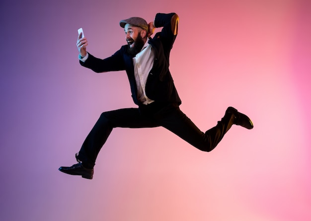 Full length portrait of happy jumping man in neon light and gradient