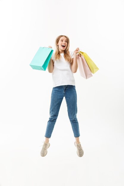 Full length portrait of a happy pretty girl holding shopping bags while jumping and looking at camera isolated over white background.