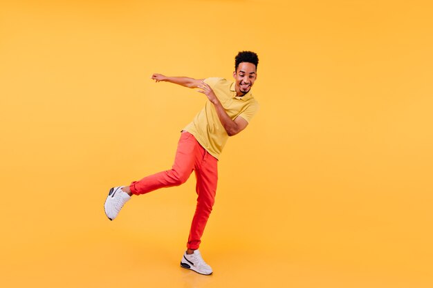 Full-length portrait of joyful african male model dancing in yellow shoes. Cheerful black man enjoying.