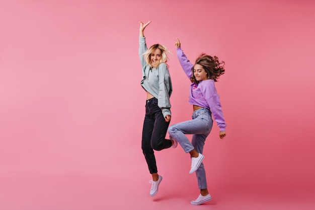 Free photo full-length portrait of jumping white girls expressing happy emotions. portrait of best friends funny dancing together.