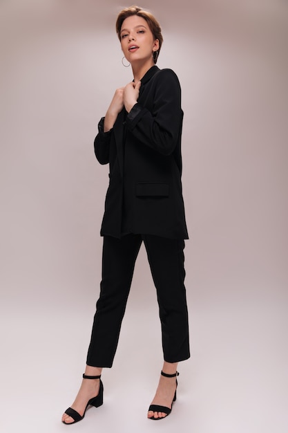 Full length portrait of lady in black suit. Attractive young woman in dark jacket and stylish pants poses on isolated background