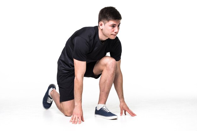 Full length portrait of a male athlete ready to run isolated on white wall