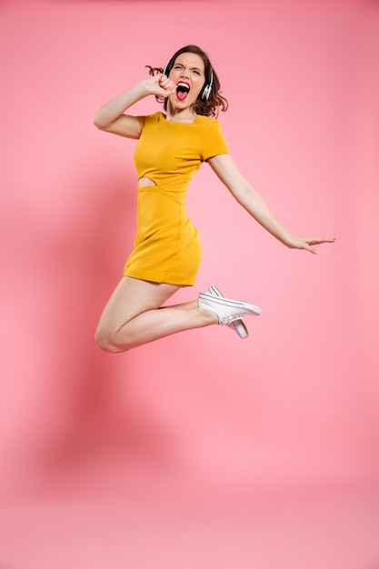 Full length portrait of pretty young woman in headphones having fun while listening to music