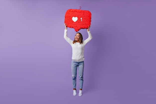 Free photo full-length portrait of stylish female blogger standing on purple. dreamy caucasian girl in white sweater dancing.