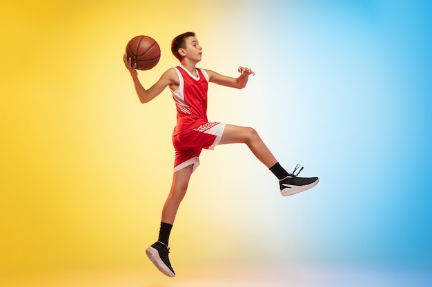 Full length portrait of a young basketball player with ball on gradient background