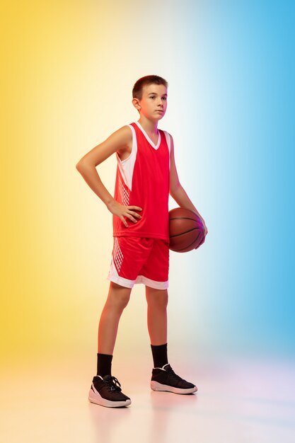 Full length portrait of a young basketball player with ball on gradient wall