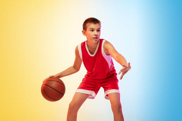 Full length portrait of a young basketball player with ball on gradient wall