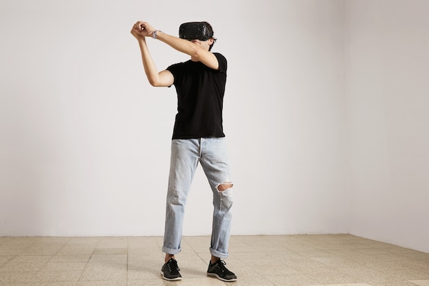 Free photo full length portrait of a young caucasian model in light blue torn jeans and black t-shirt playing baseball or tennis in vr glasses