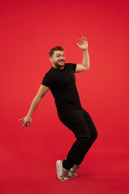 Free photo full length portrait of young high jumping man isolated on red  wall. male caucasian model. copyspace. human emotions, facial expression, sport concept.